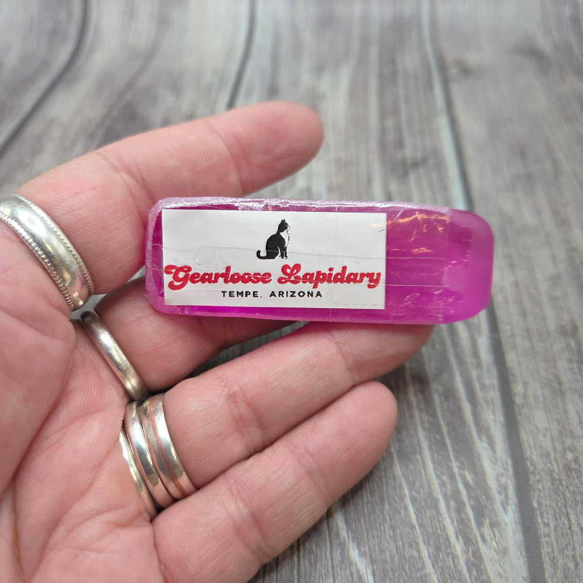 Pink corundum Boule Tool™ resting across a hand, showing the Gearloose Lapidary label